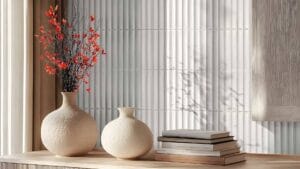 Vases with decorative branches and books on a wooden surface with textured tile wall background, showcasing modern interior design accents.