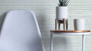 Modern minimalist interior with white tiled wall, sleek white chair, small wooden table, stylish potted plant, and Starbucks mug, exemplifying contemporary home decor and office styling.