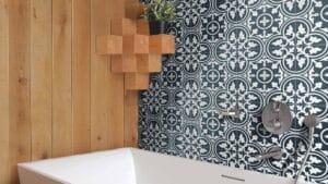 Bright bathroom with geometric patterned blue and white tiles, wooden accents, modern fixtures, and a cozy potted plant for stylish home renovation.