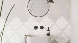 Smooth white bathtub with black wall-mounted faucet and soap dispenser, modern bathroom design with geometric patterned tiles, minimalist decor, and a round mirror on a white wall for a sleek aesthetic.