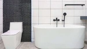 Sleek modern bathroom with white freestanding bathtub, black matte fixtures, and a minimalist design featuring white tiled walls and a black tiled accent wall.