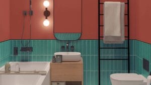 Modern bathroom with coral walls, green tile wainscoting, and black fixtures including a towel rack, wall-mounted lighting, and a black ladder towel rail. Features a white bathtub, vessel sink on a wooden vanity, and toilet.