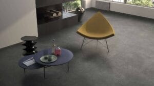 Sleek modern living room with contemporary furniture and polished tile flooring, featuring a mustard-colored lounge chair, black side table with decorative bottles, and a dark coffee table with books and glassware.