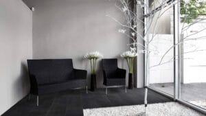 Modern waiting area with black rattan furniture, white decorative flowers, and minimalist decor featuring large glass windows and contemporary design elements.