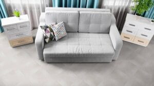 Soft grey fabric sofa with two decorative geometric patterned pillows, flanked by white modern side tables with plants, in a bright, stylish living room setting.