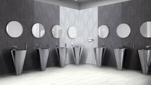 Sleek modern bathroom with stainless steel pedestal sinks and large round mirrors, stylish gray tiled walls, contemporary fixtures, ideal for a bathroom renovation or commercial restroom design.