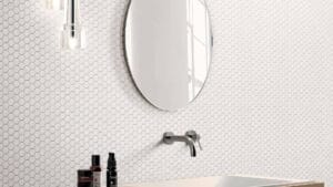 Sleek bathroom with white hexagon tile wall, modern wall-mounted faucet, oval mirror, and skincare products, perfect for bathroom renovation and interior design.