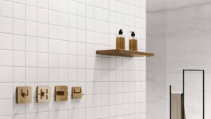 Sleek modern shower with gold fixtures, white tiled walls, and a minimalist wooden shelf with soap dispensers, ideal for contemporary bathroom renovations.