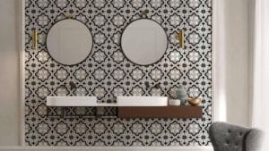 Modern bathroom wall with black, white, and gray patterned tile, featuring two round mirrors, gold wall sconces, and a sleek wooden floating vanity with stylish decor elements.
