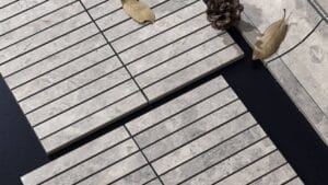 Natural stone grey tiles arranged in a modern outdoor patio setting with decorative pinecone and dried leaves. Perfect for garden pathways or home alfresco areas.
