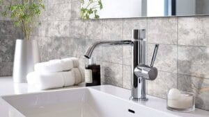 Modern chrome bathroom faucet with sleek design and a single lever, set against a textured grey stone tile wall. Perfect for enhancing contemporary bathroom decor.