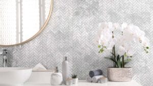Elegant bathroom interior featuring a textured herringbone tile wall, white ceramic sink, decorative orchid plant, and modern toiletries, showcasing quality building supplies from Builders Warehouse Online.