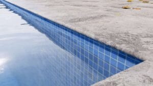 Pool edge with blue tile lining and concrete deck, showcasing backyard swimming pool design and waterproofing features.