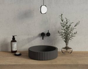 Black modern vessel sink with matte finish, mounted on wooden bathroom vanity with black fixtures and decorative plant, ideal for contemporary bathroom renovations.