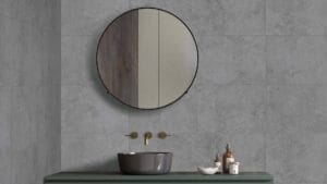 Modern bathroom vanity with round mirror, grey vessel sink, wall-mounted gold faucet, and bathroom accessories on a sleek green countertop. Perfect for contemporary bathroom designs.