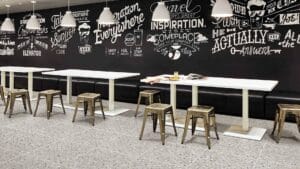 Bright, modern cafe interior with white tables, metallic stools, and a black wall featuring inspirational chalkboard-style typography, ideal for stylish commercial or residential spaces.