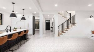 Modern open-plan kitchen and living room with sleek cabinetry, black accents, and a staircase featuring black railings and wooden steps, showcasing stylish home renovation ideas.