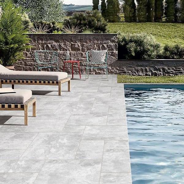 Slate grey outdoor tiling next to swimming pool with garden furniture and lush landscaping. Perfect for poolside patios and backyard renovations, offering durable and stylish paving options.