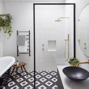 A modern bathroom shower area with black framing, white tiled walls, black and white geometric floor pattern, and contemporary fixtures.