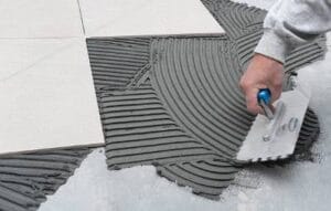High-quality grey tile adhesive being applied on the floor using a notched trowel for professional flooring installation.