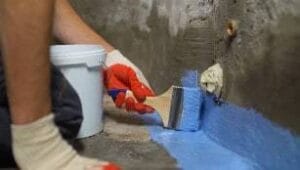 Flexible waterproofing membrane being applied to a concrete surface with a trowel and brush.